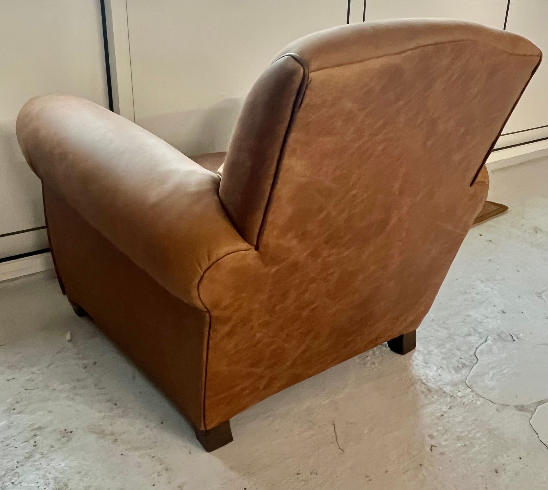 Un fauteuil en cuir beige placé en diagonale contre un mur, sur un sol gris clair.