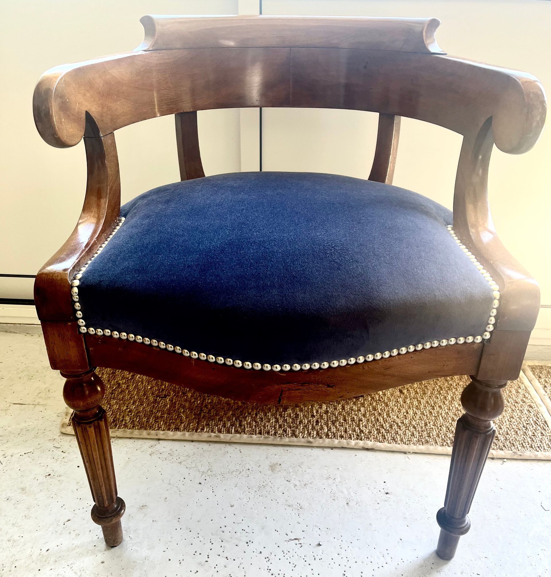 Un fauteuil en bois au dossier incurvé, recouvert d'un tissu bleu foncé et orné de clous décoratifs argentés.