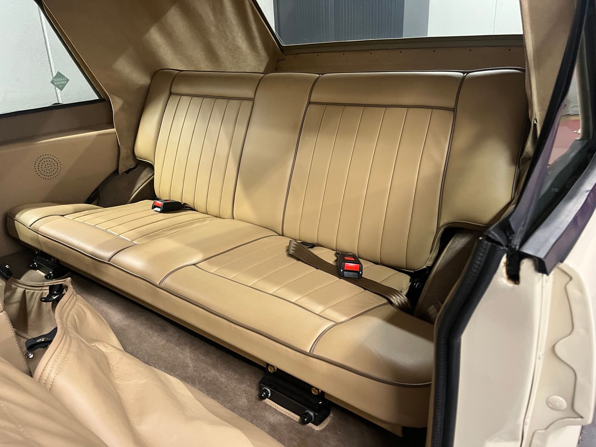 Siège arrière en cuir beige plissé d'un véhicule décapotable, avec ceintures de sécurité et panneaux intérieurs visibles.