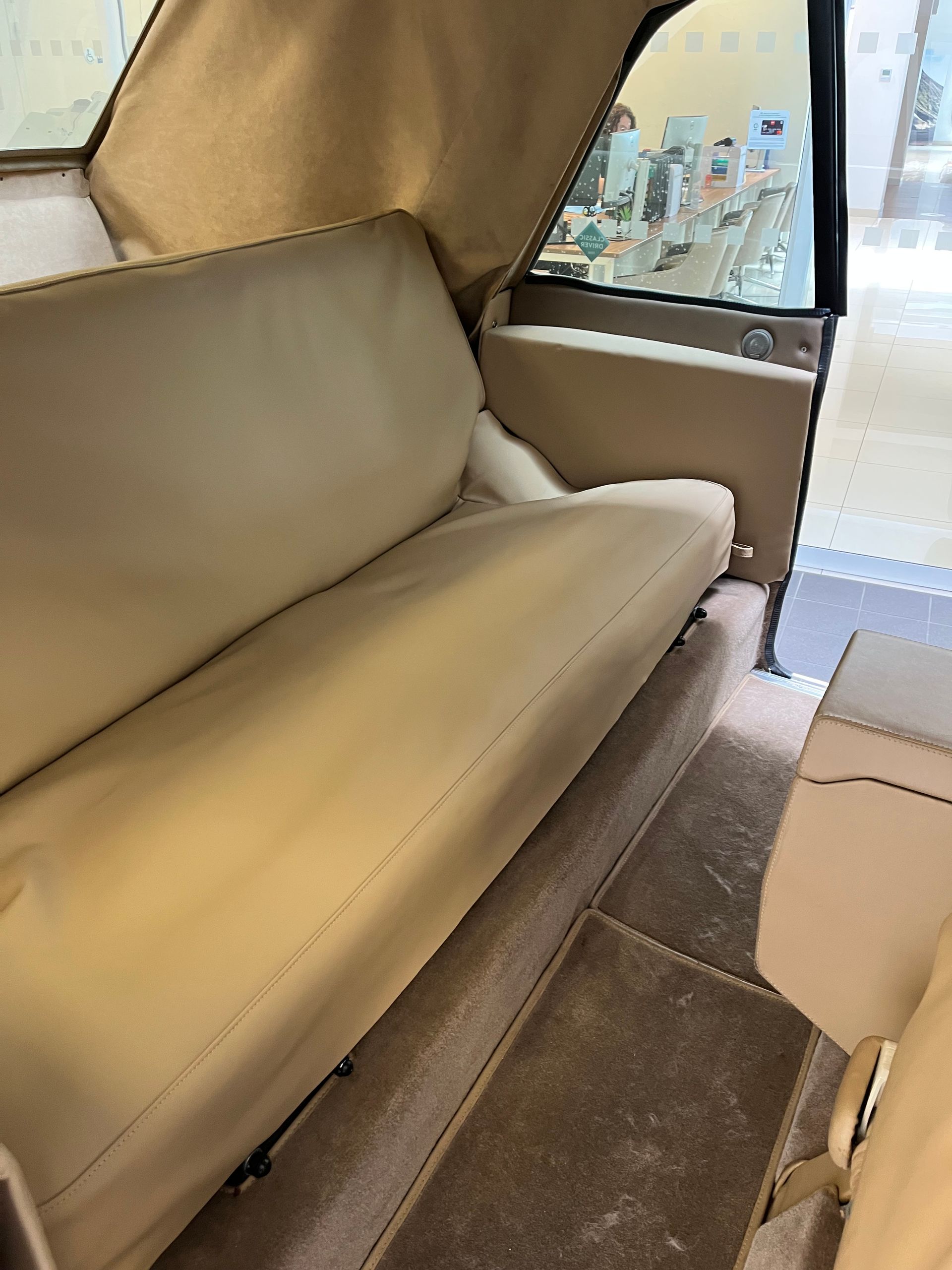 Intérieur beige d'une voiture avec une longue banquette, sellerie assortie et moquette marron.