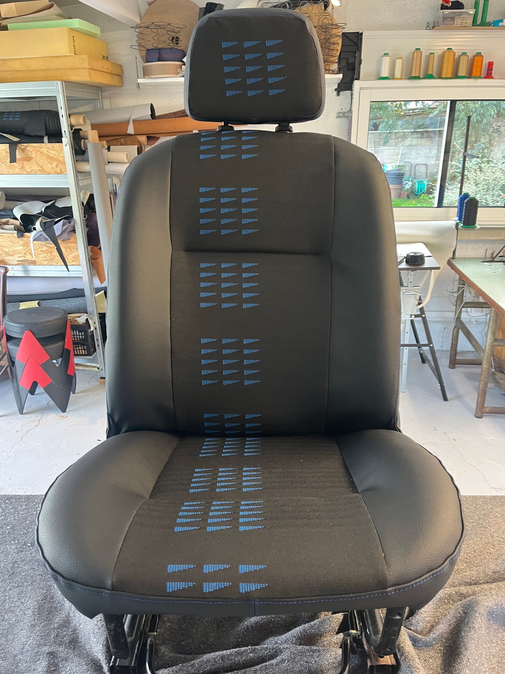 Un siège de véhicule noir dans un atelier, avec une bande verticale bleue.