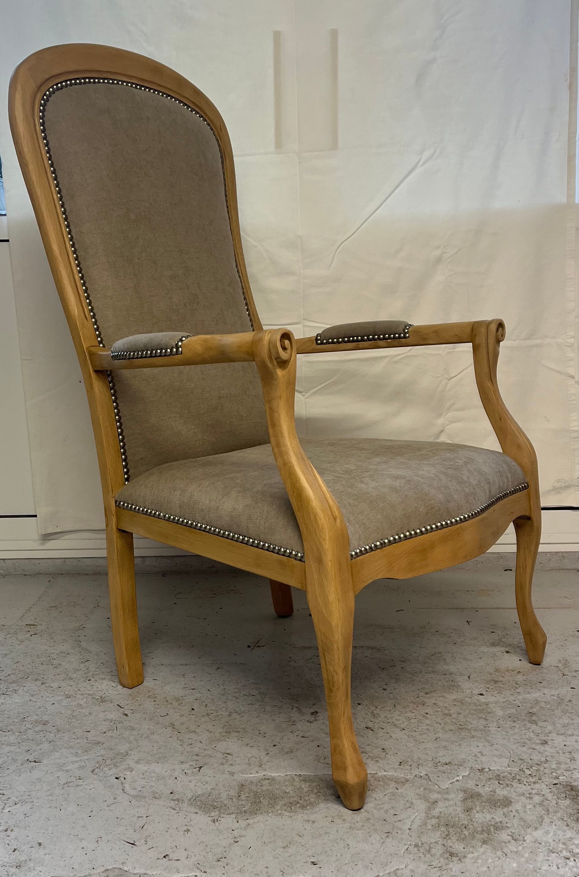 Un fauteuil à dossier haut en bois clair, avec assise et dossier rembourrés beiges, orné de clous décoratifs en métal.