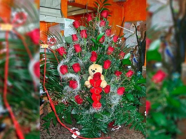 Un ramo de rosas rojas con un osito de peluche en el medio.