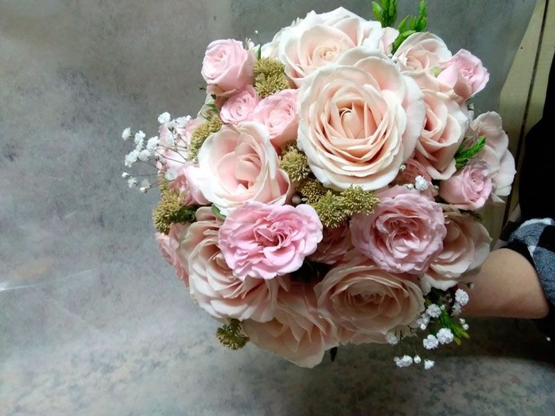 Una persona sostiene un ramo de rosas rosadas y aliento de bebé.