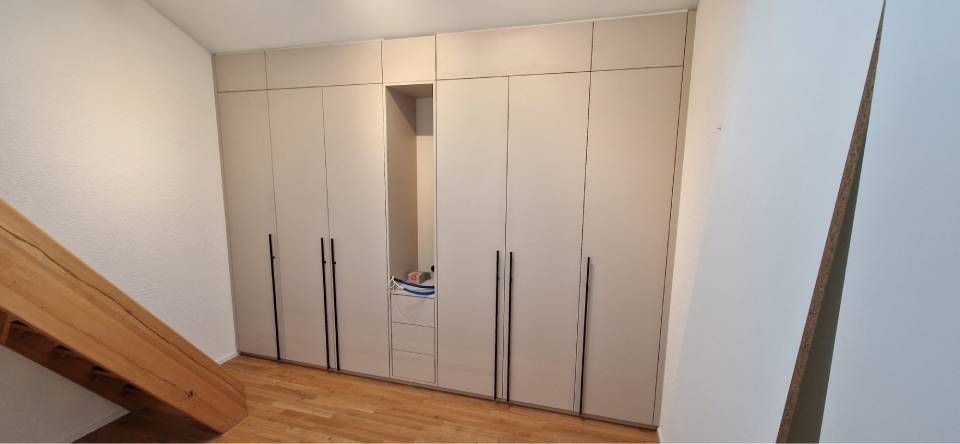 Leeres, weiss gestrichenes Lagerhausinterieur mit hohen Fenstern auf der rechten Seite und grossen Stützsäulen.