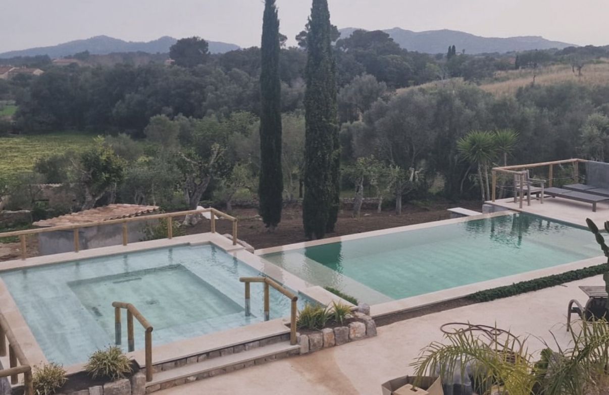 Dos piscinas rectangulares, una vacía, con una valla de madera, dan a un paisaje verde.