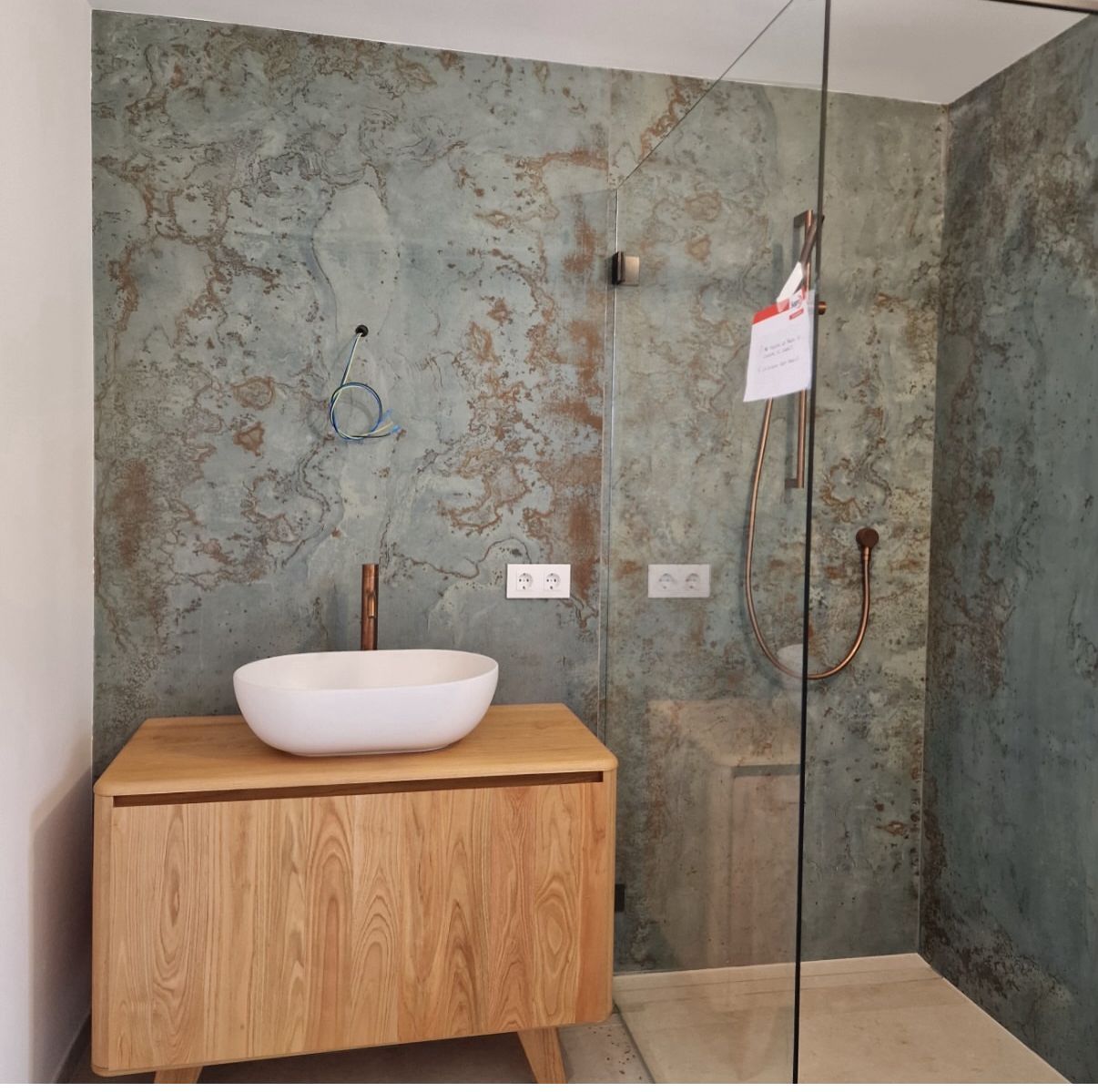 Baño con tocador de madera, lavabo ovalado y ducha a ras de suelo con paredes texturizadas en color azul verdoso.