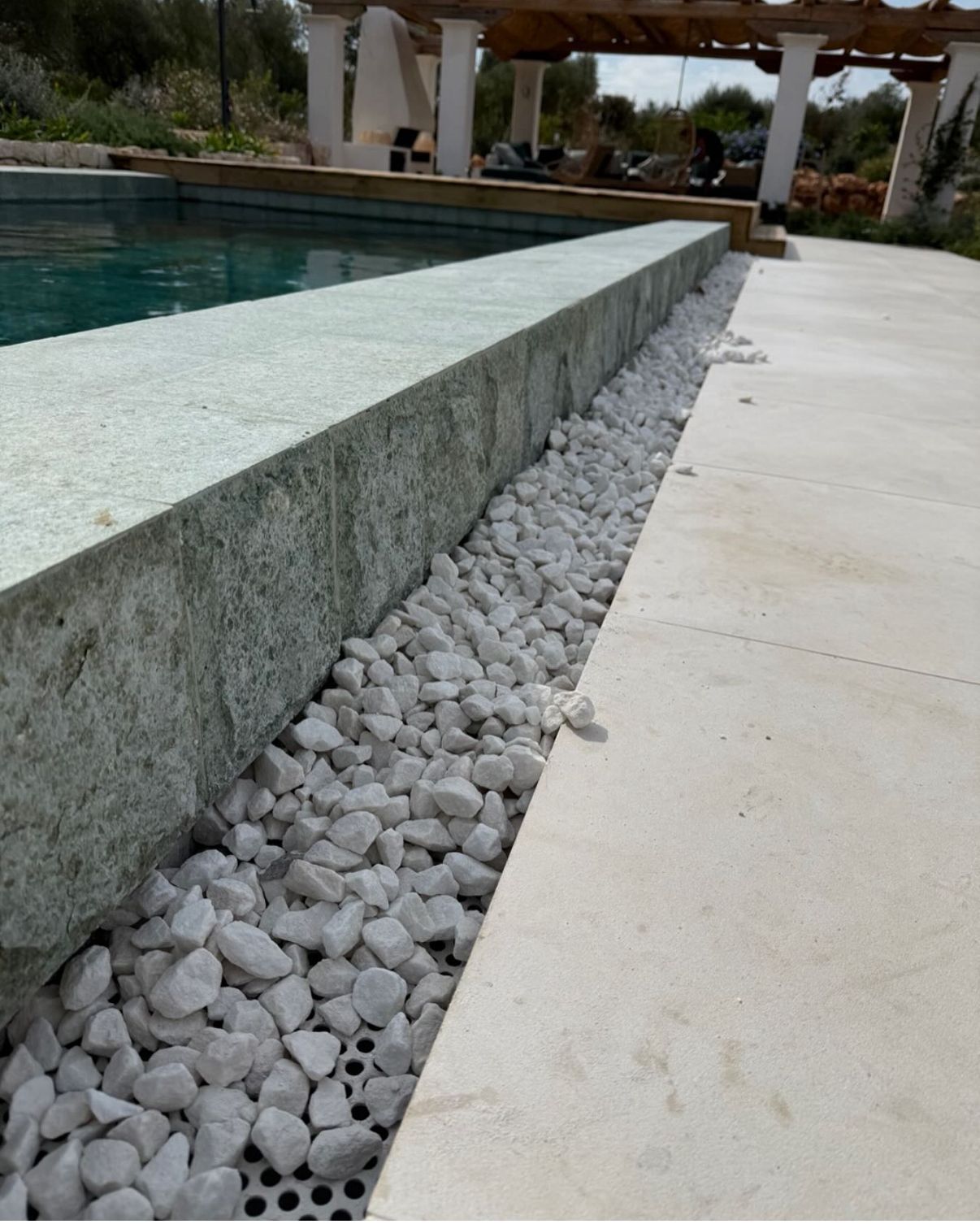 Zona de piscina con bordes de piedra, grava blanca y pavimento de color claro.