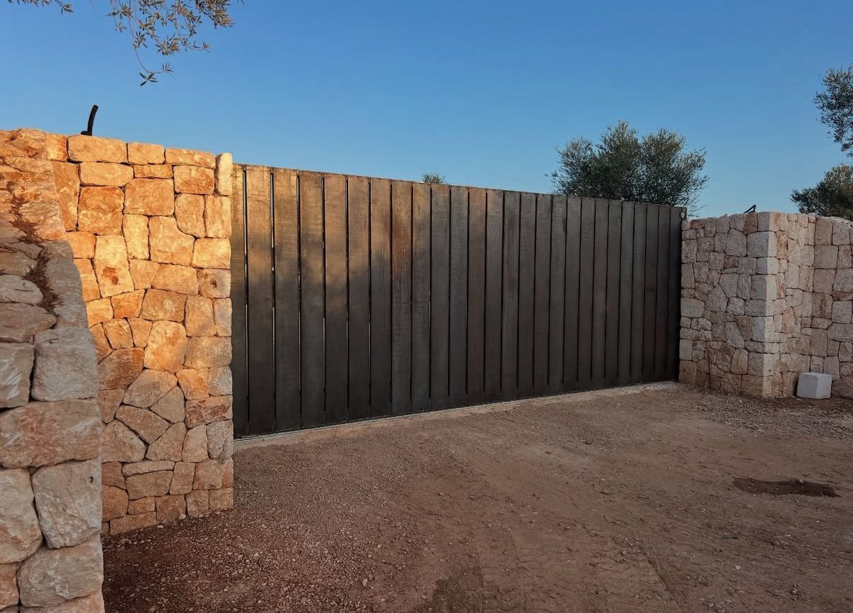 Muros de piedra flanquean una puerta de madera desgastada en un camino de grava bajo un cielo azul despejado.