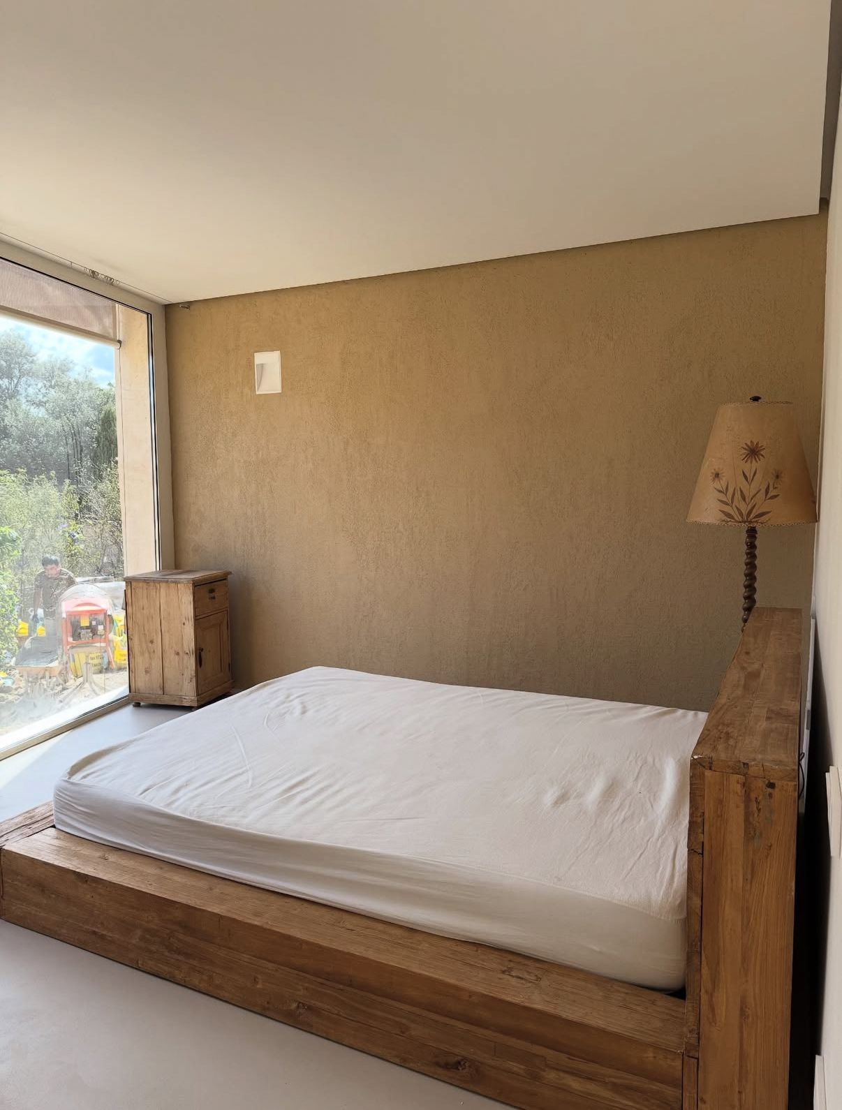 Dormitorio con cama de madera, ropa de cama blanca y mesita de noche cerca de una ventana grande.
