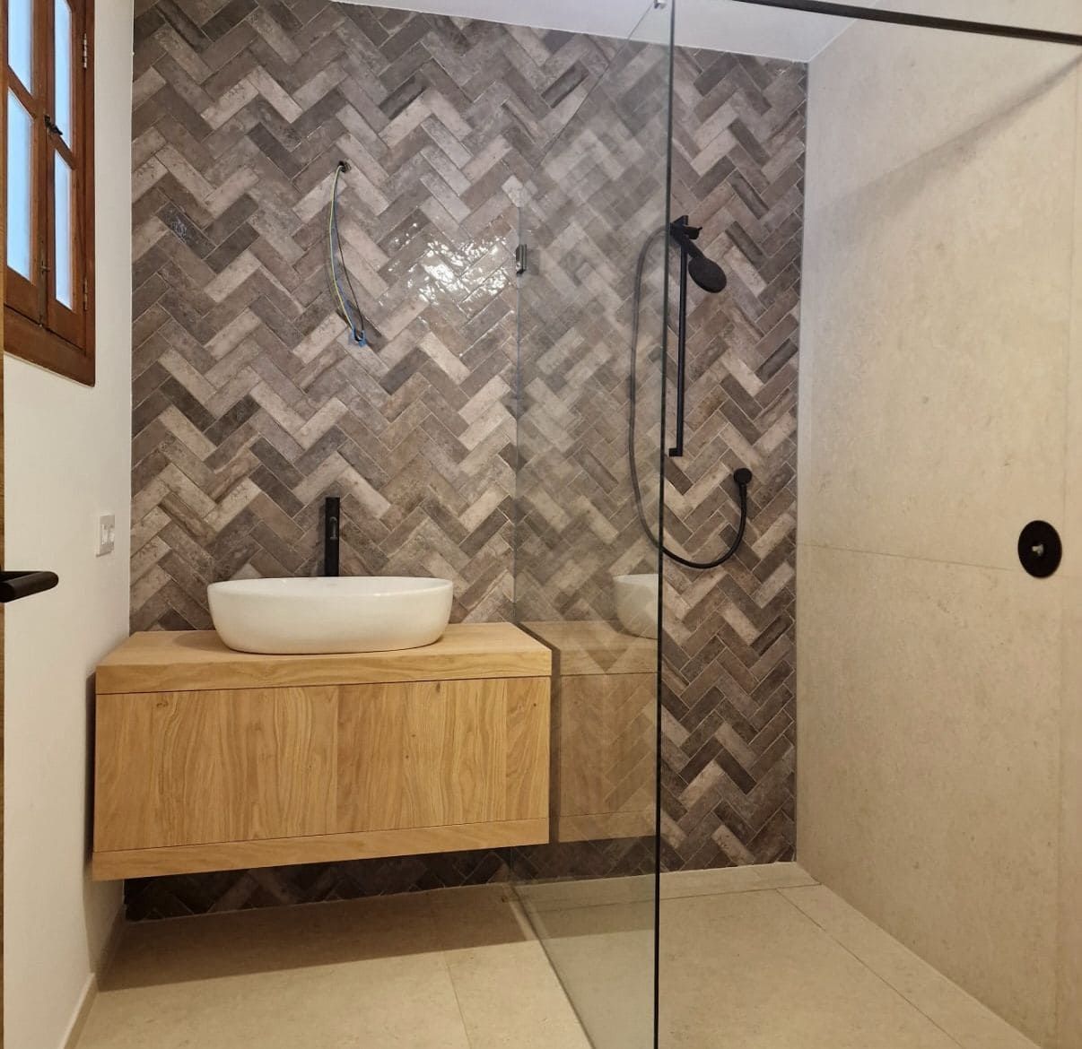 Baño con tocador de madera y pared decorativa con azulejos en espiga. Cabina de ducha de cristal.