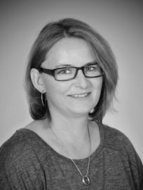 Eine Frau mit Brille und Halskette lächelt auf einem Schwarzweißfoto.