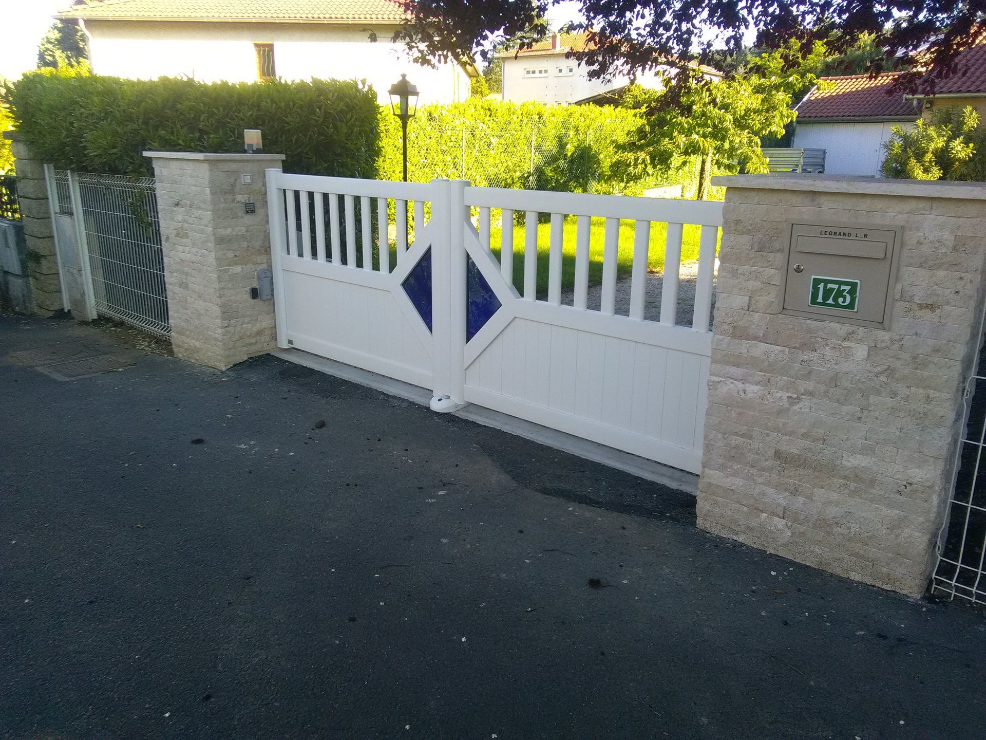 Un portail double blanc orné de losanges bleus, encadré par deux piliers de pierre avec une boîte aux lettres.