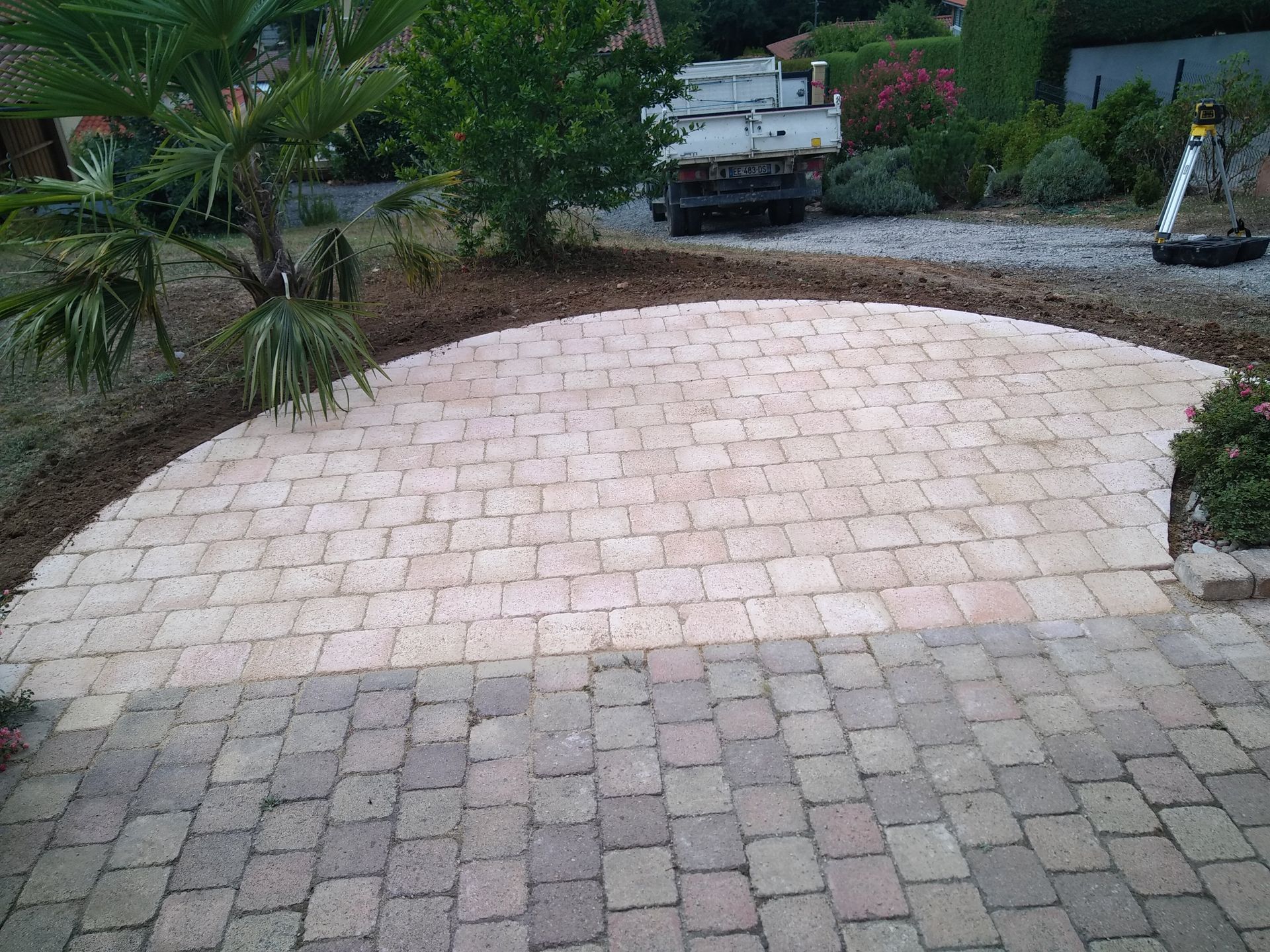 Une terrasse partiellement achevée, composée de pavés en pierre beige clair, faisant la transition avec une surface existante en pierre gris foncé.