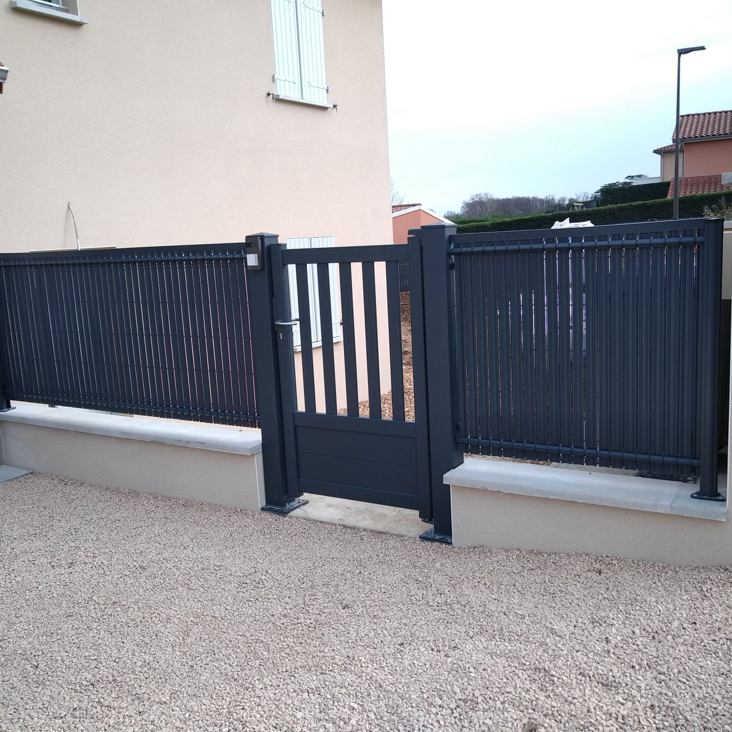 Un portillon piétonnier en métal sombre entre deux sections de clôture décorative.