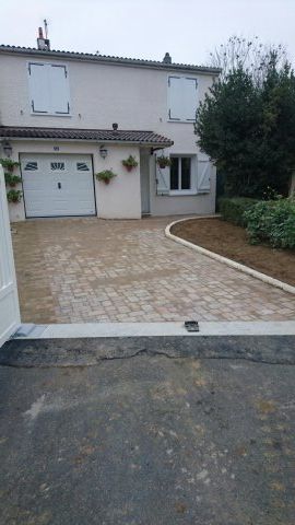 Une maison beige à deux étages avec une porte de garage blanche et une allée en pierre fraîchement pavée.