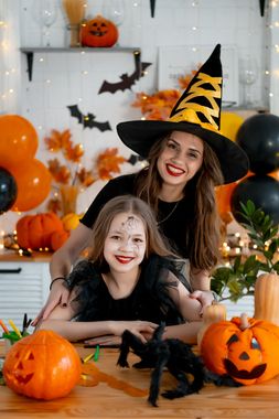 Dwie osoby w kostiumach na Halloween pozujące z dyniami i nietoperzami w świątecznej, pomarańczowo-czarnej scenerii