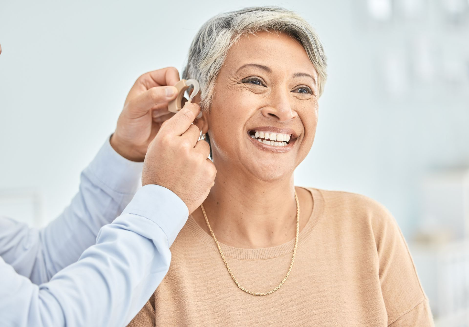 Un femme souriante essaye un appareil auditif en contour d'oreille