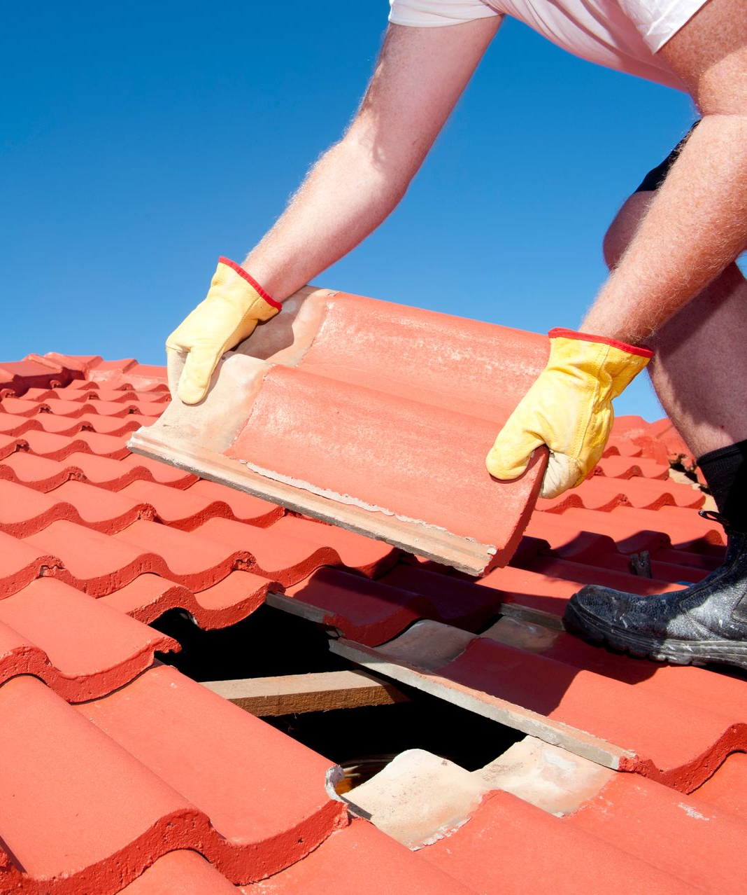 Une personne portant des gants jaunes remplace une tuile rouge par une journée ensoleillée.
