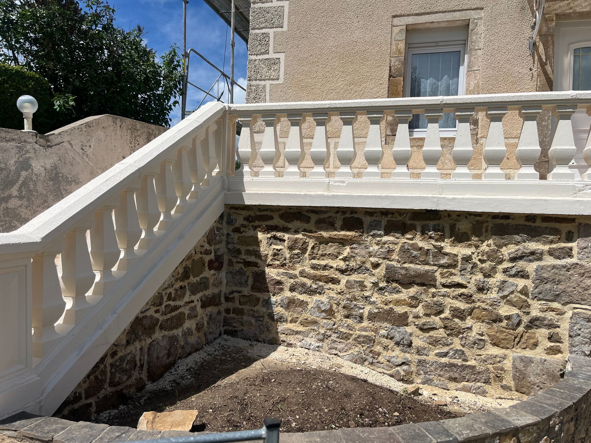 Mur de pierre avec balustrade blanche et escalier, à côté d'un bâtiment.