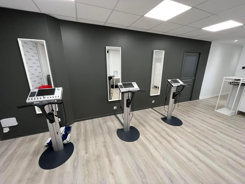 Studio de fitness avec trois appareils vibrants, des miroirs muraux et un parquet gris clair.