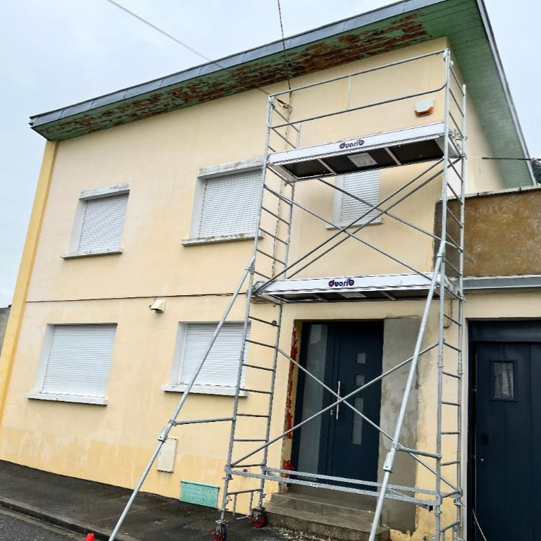 Échafaudage devant une maison beige de deux étages avec une porte grise.