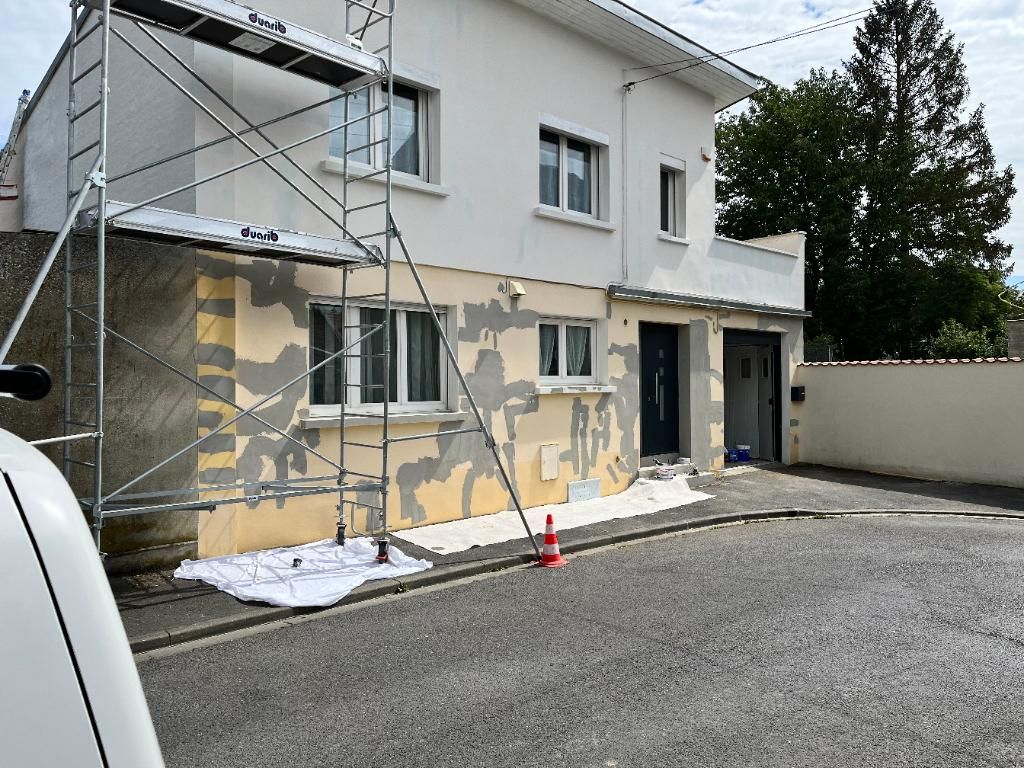 Façade de la maison en rénovation avec des échafaudages ; peinture écaillée visible sur un mur jaune.
