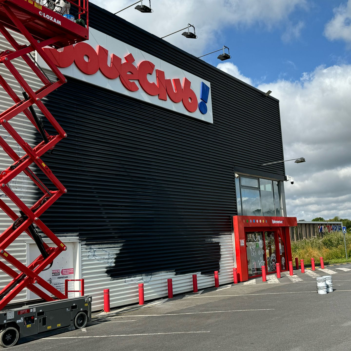 Le mur noir de JouéClub en cours de peinture avec une nacelle rouge.