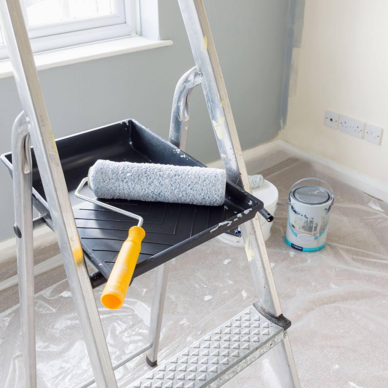 Échelle avec rouleau à peinture dans un bac, pots de peinture, bâche en plastique au sol.