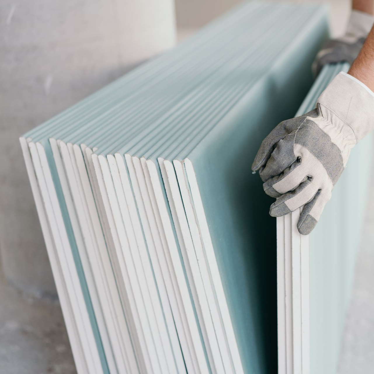 Une personne portant des gants tient une pile de plaques de plâtre.