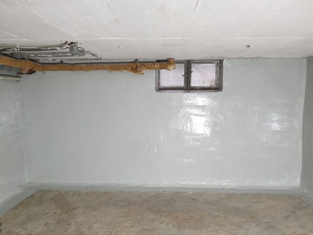 Kellerinnenraum mit frisch gestrichenen grauen Wänden, einem kleinen Fenster und freiliegenden Rohren in der Nähe der Decke.