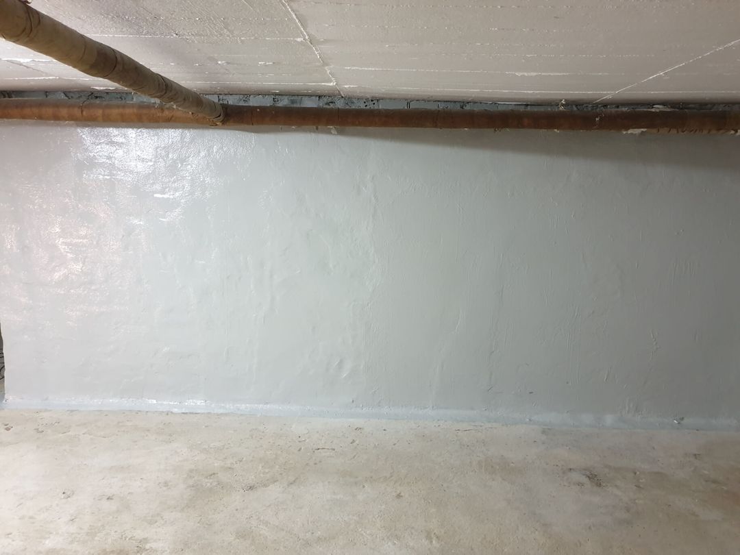 Ein Betonraum mit weiß gestrichener Wand und Decke, über die oben ein braunes Rohr verläuft.