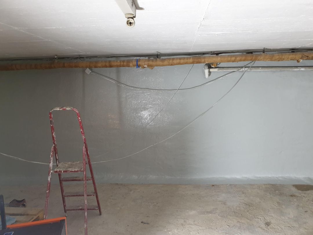 In einem Keller steht neben einer hellgrau gestrichenen Wand eine Leiter. Über ihr sind Kabel gespannt.