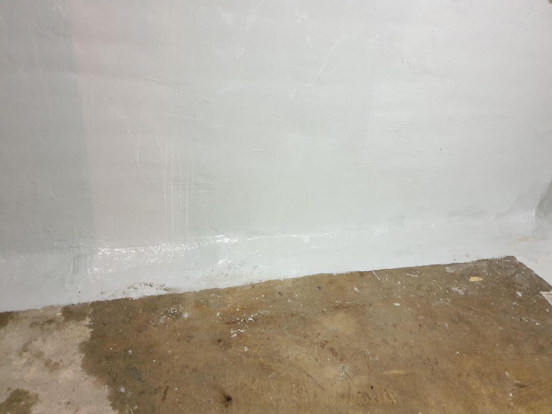 Weiß gestrichene Wand trifft auf fleckigen Betonboden; Wasserflecken sind sichtbar.