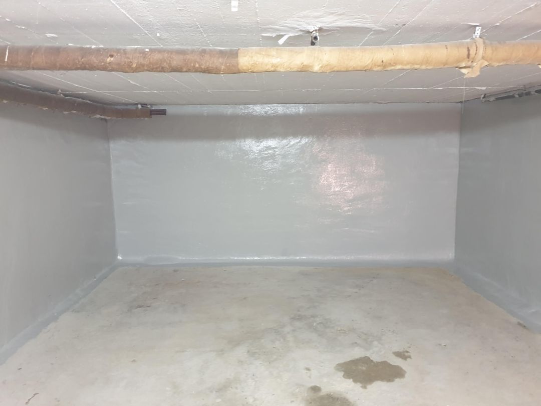 Grau gestrichene Kellerwände und -decke. Über der Decke verläuft ein Rohr. Der Boden hat einen Wasserfleck.