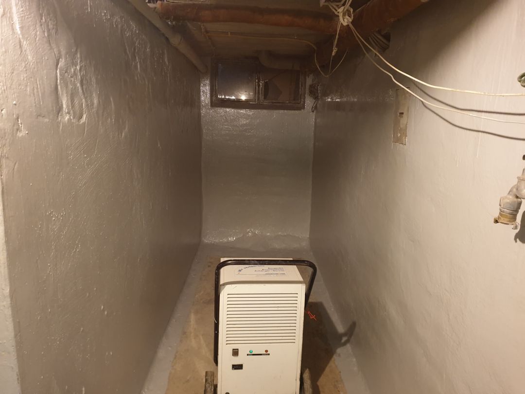 Ein kleiner Kellerraum mit weißen Wänden und einem Luftentfeuchter; Licht kommt aus der Mitte.