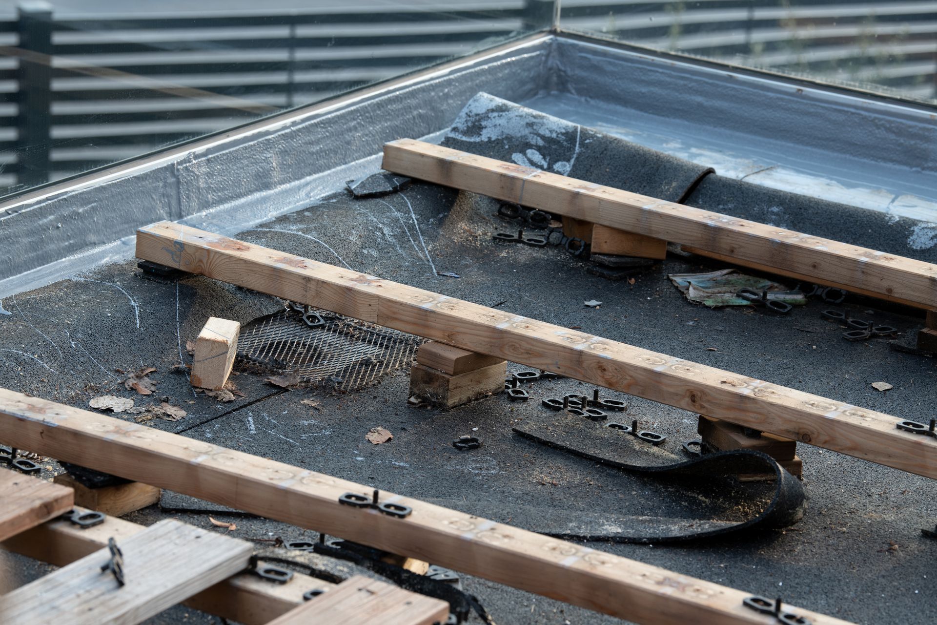 Flachdach mit Holzbalken und Befestigungen, mit dunklem Material verkleidet, im Außenbereich.