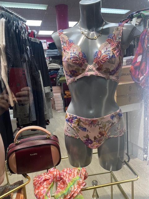 Boutique de vêtements avec des manteaux sur des portants et des sacs à main exposés sur des étagères et des tables.