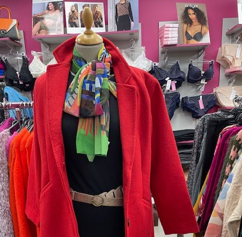 Manteau sur un mannequin dans un magasin de vêtements, accompagné d’une écharpe et d’une ceinture.