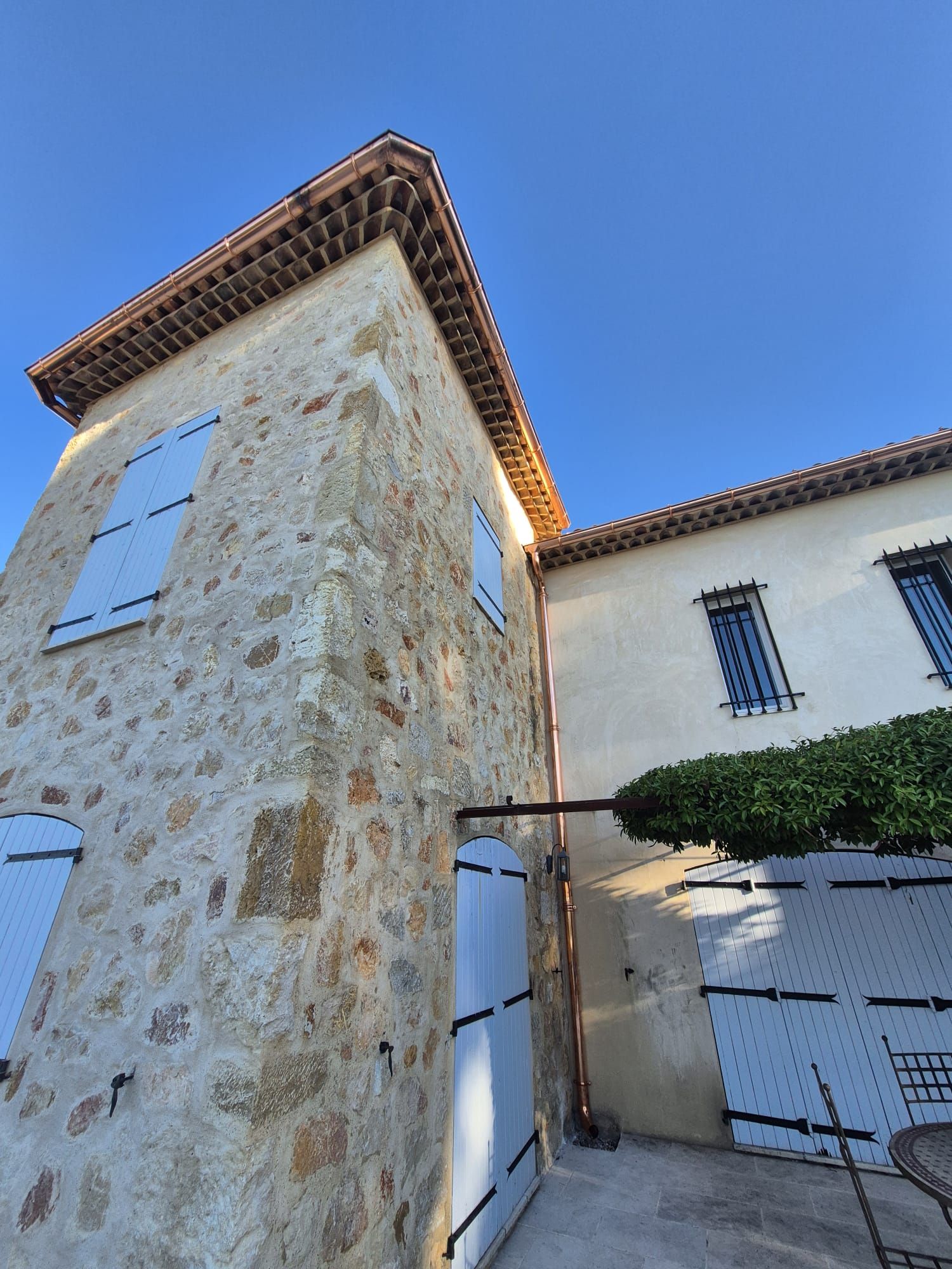 Bâtiment en pierre aux volets bleus, sous un ciel d'un bleu limpide.