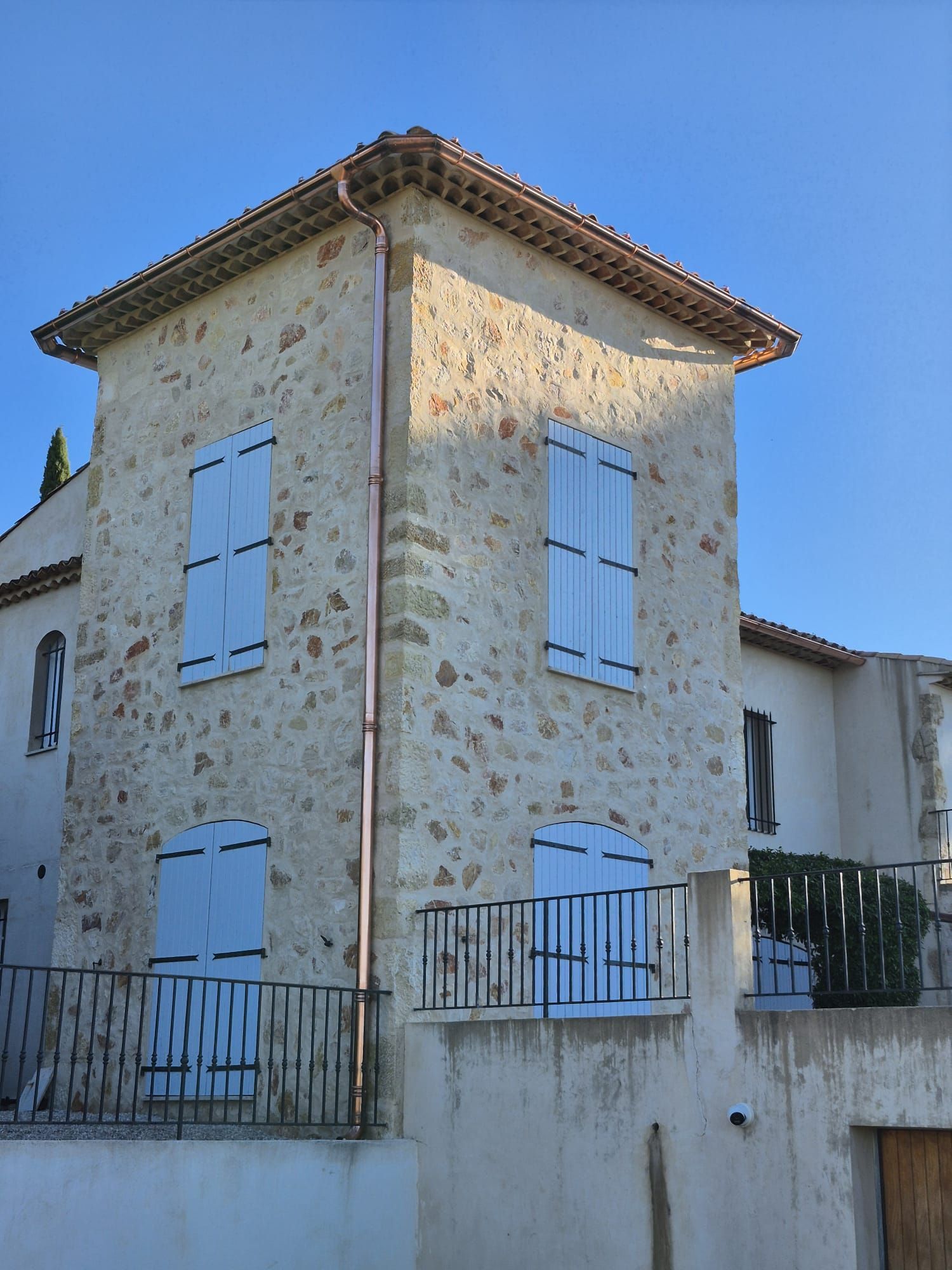 Bâtiment en pierre aux volets bleu clair et aux gouttières en cuivre, se détachant sur un ciel bleu.