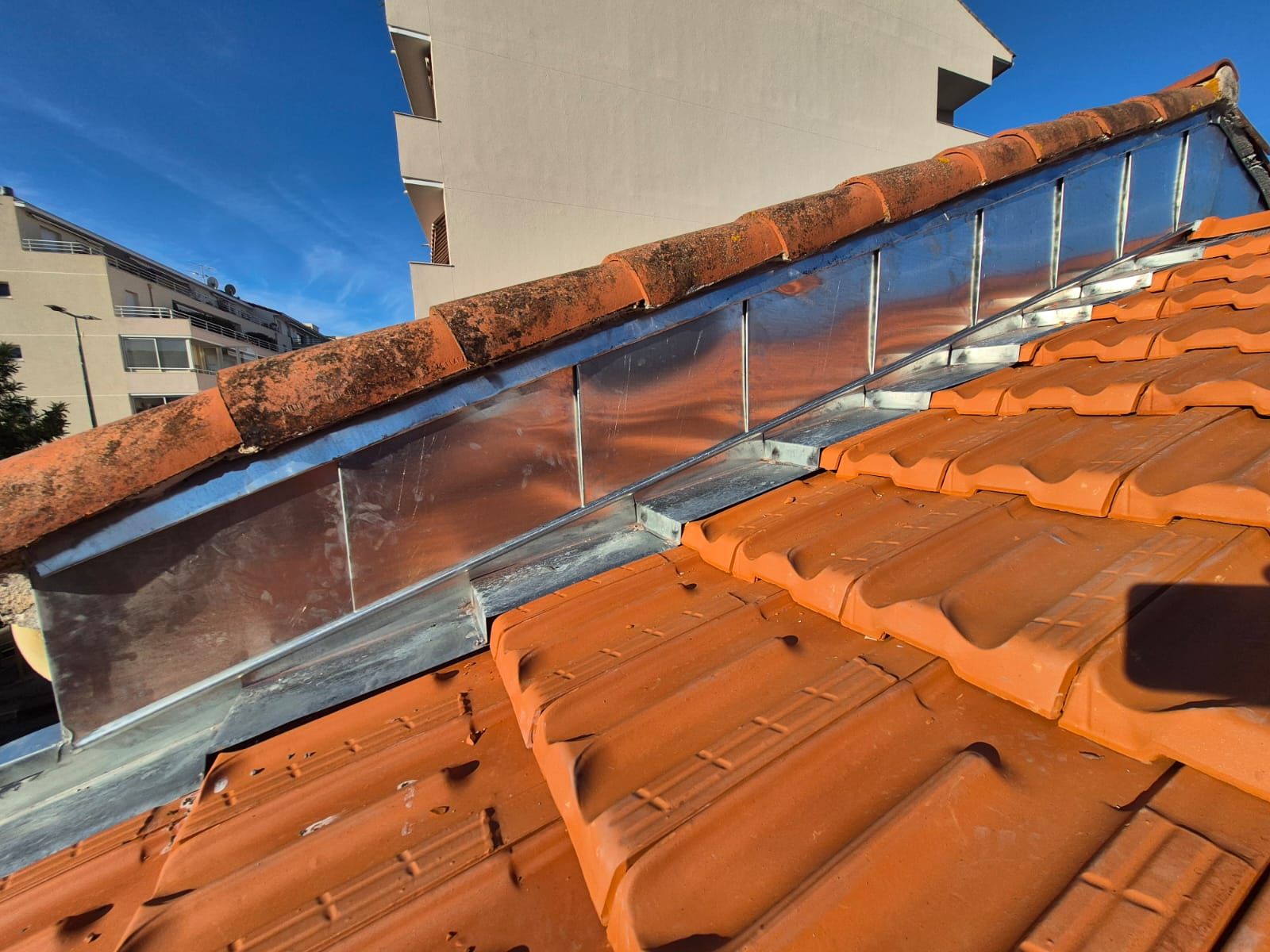Gros plan sur un toit de tuiles rouges avec une bande métallique à la jonction avec un mur.
