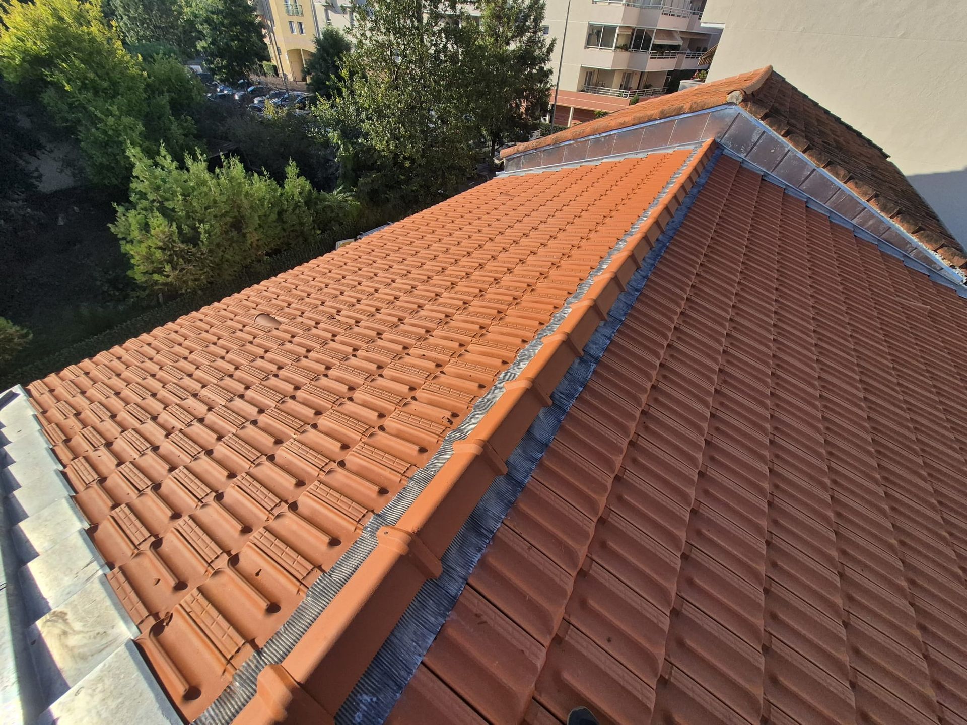 Toiture en tuiles rouges d'un bâtiment, avec des solins métalliques apparents sur les bords.