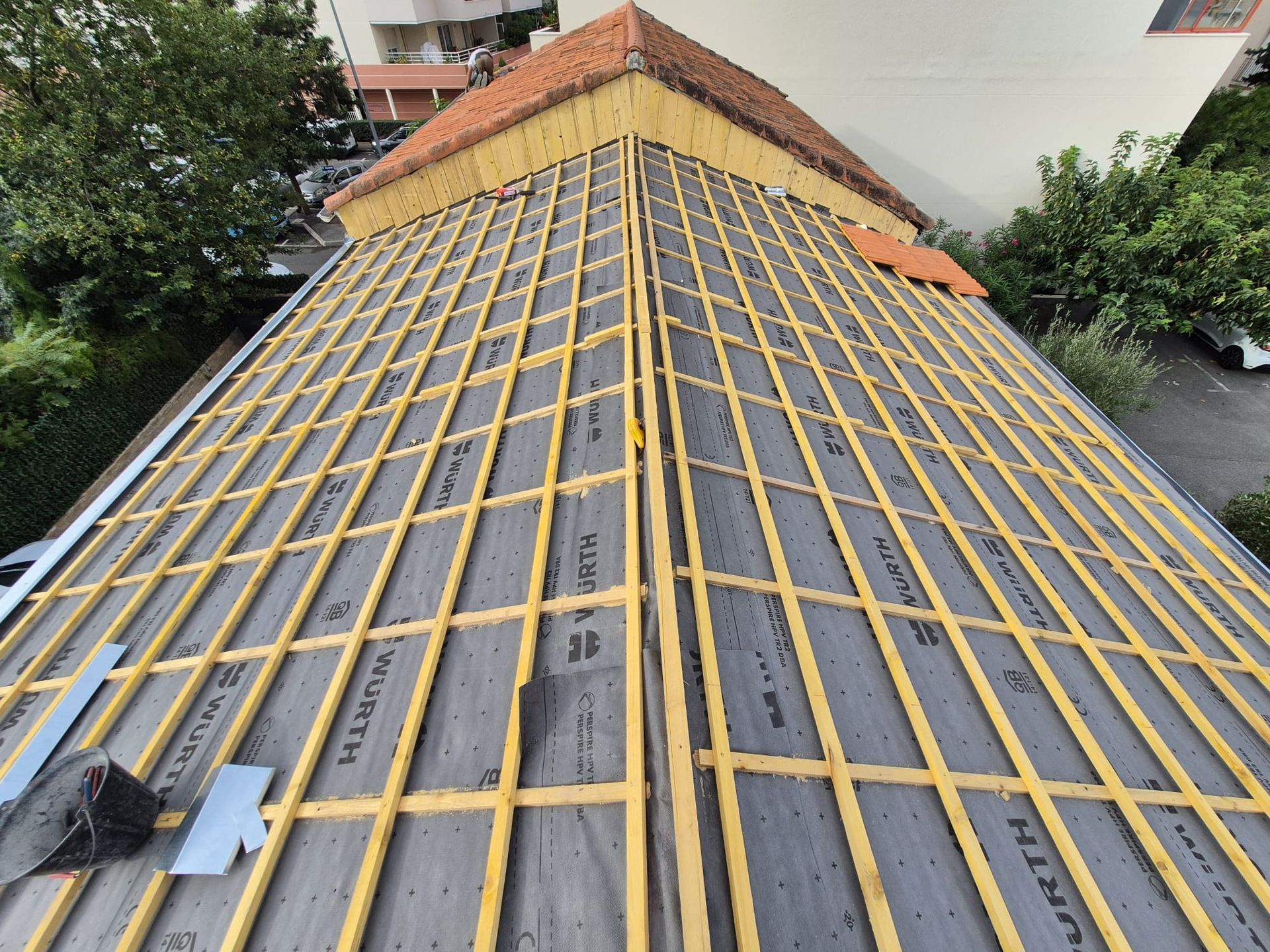 Toiture en construction, chevrons en bois, sous-couche noire et solins métalliques sur un bâtiment.