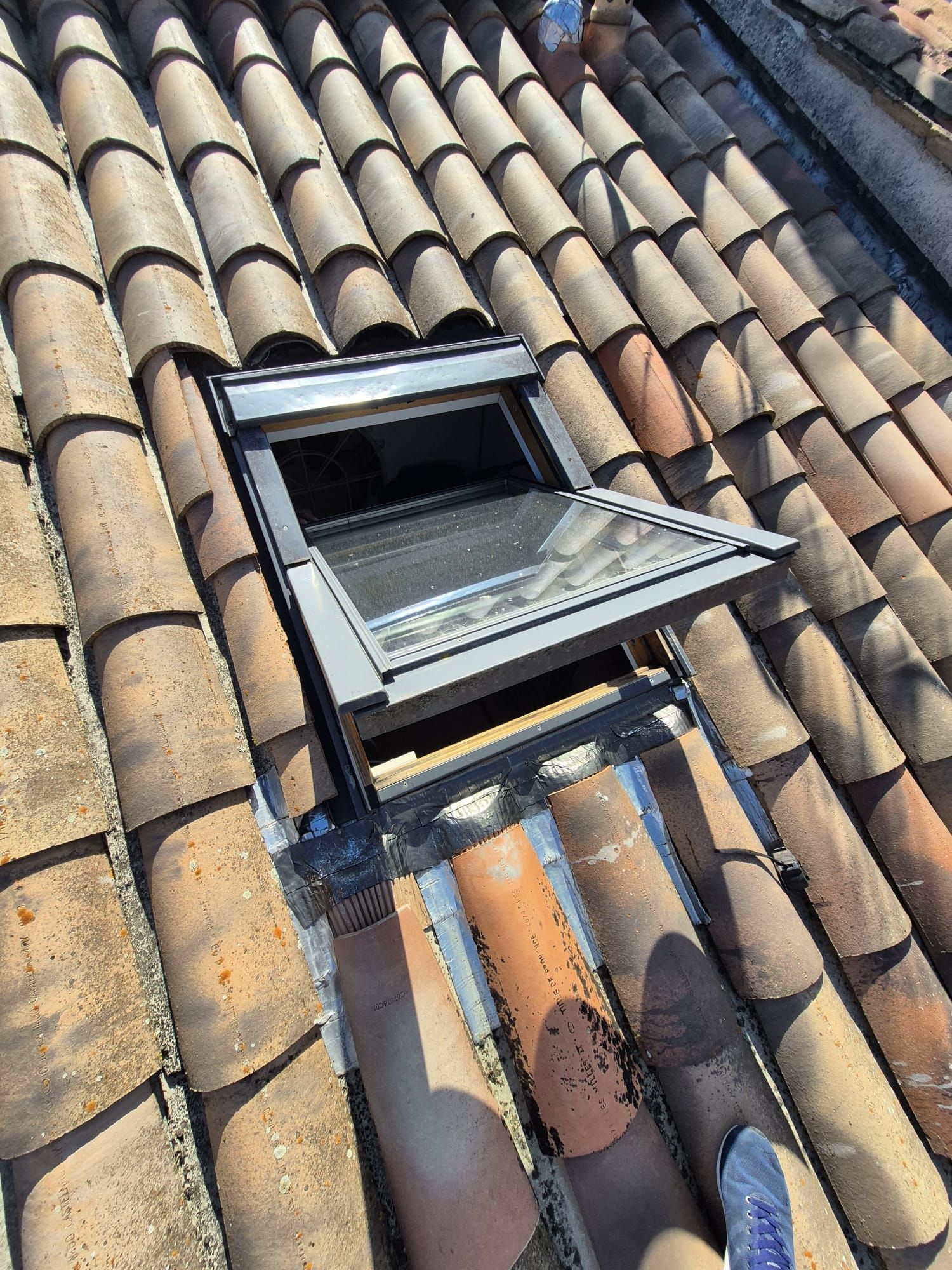 Puits de lumière ouvert sur un toit de tuiles en terre cuite, laissant apparaître un écran en treillis.