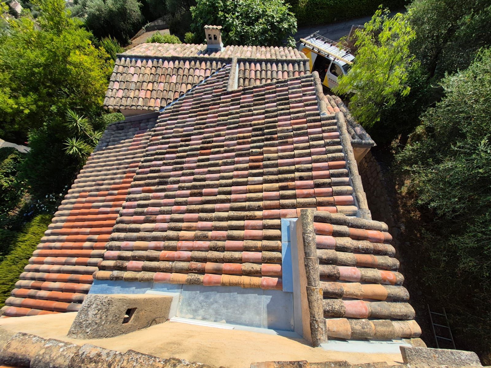 Vue aérienne d'un toit de tuiles rouges sur un bâtiment, entouré d'arbres verts dans un cadre ensoleillé.