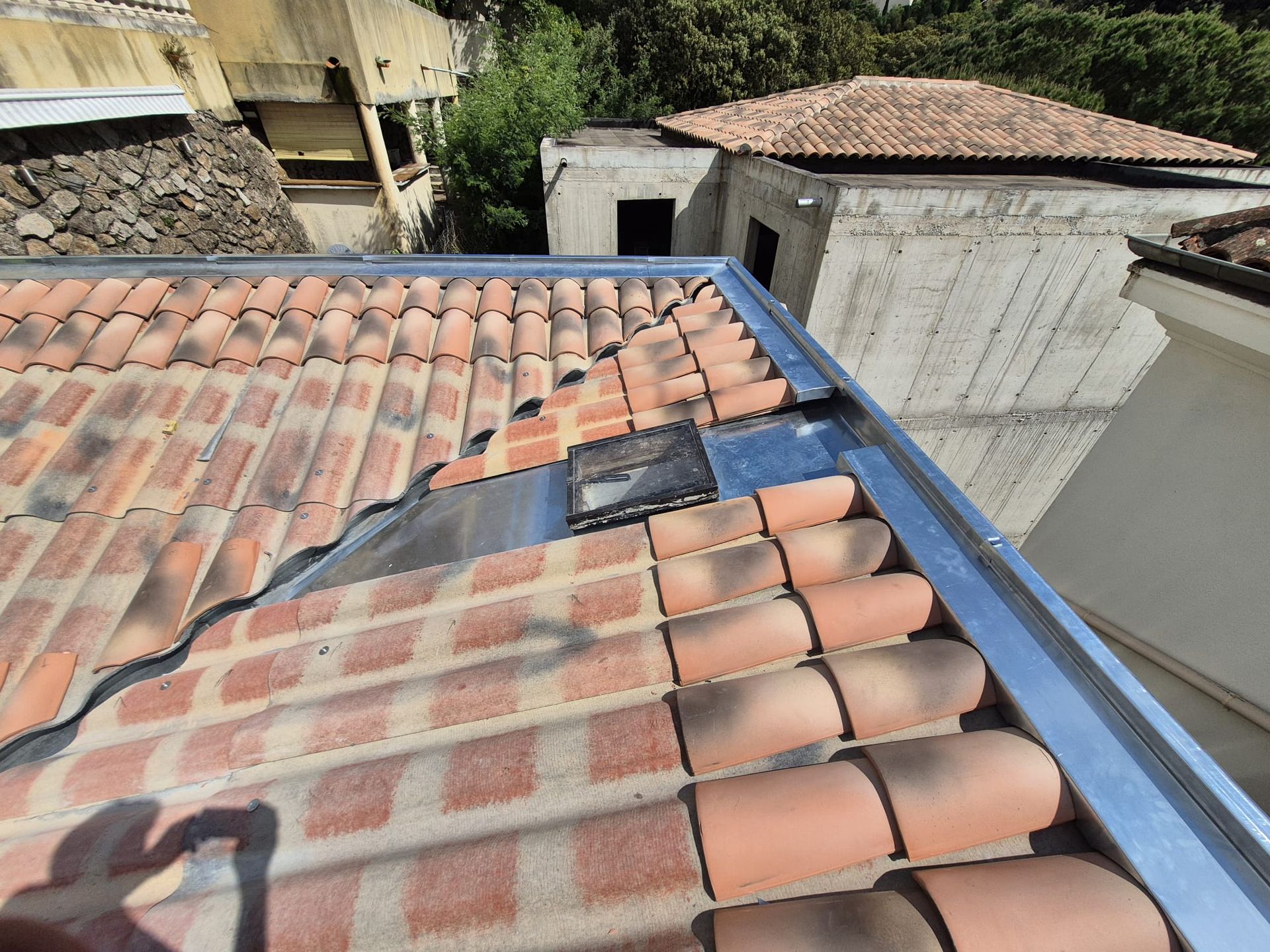 Toiture en tuiles de terre cuite orange, partie endommagée et gouttière argentée au soleil.