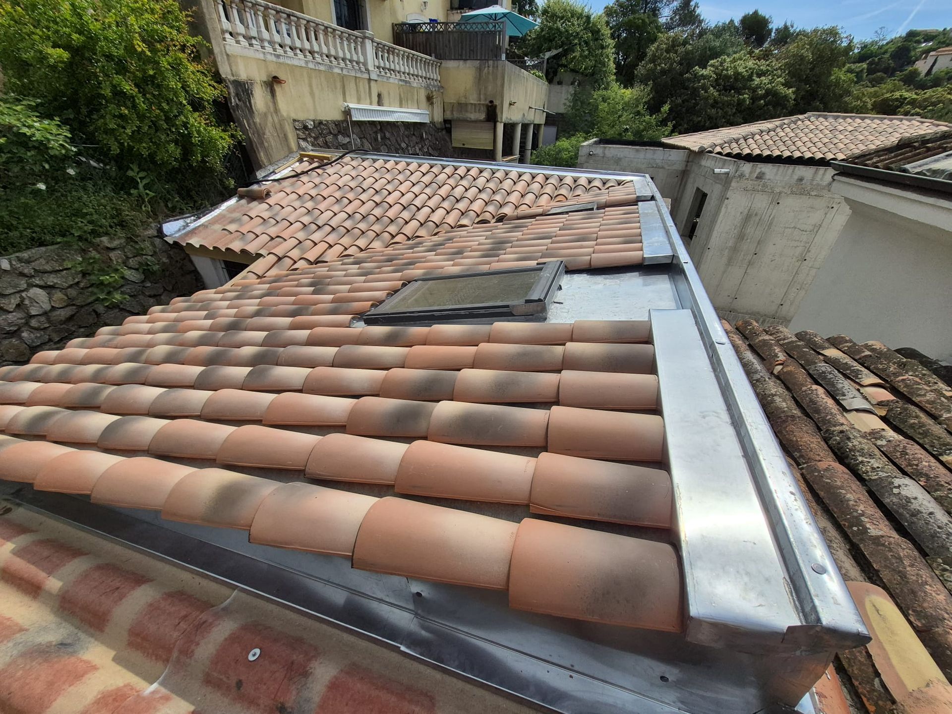 Toiture en tuiles de terre cuite avec puits de lumière et solins métalliques.