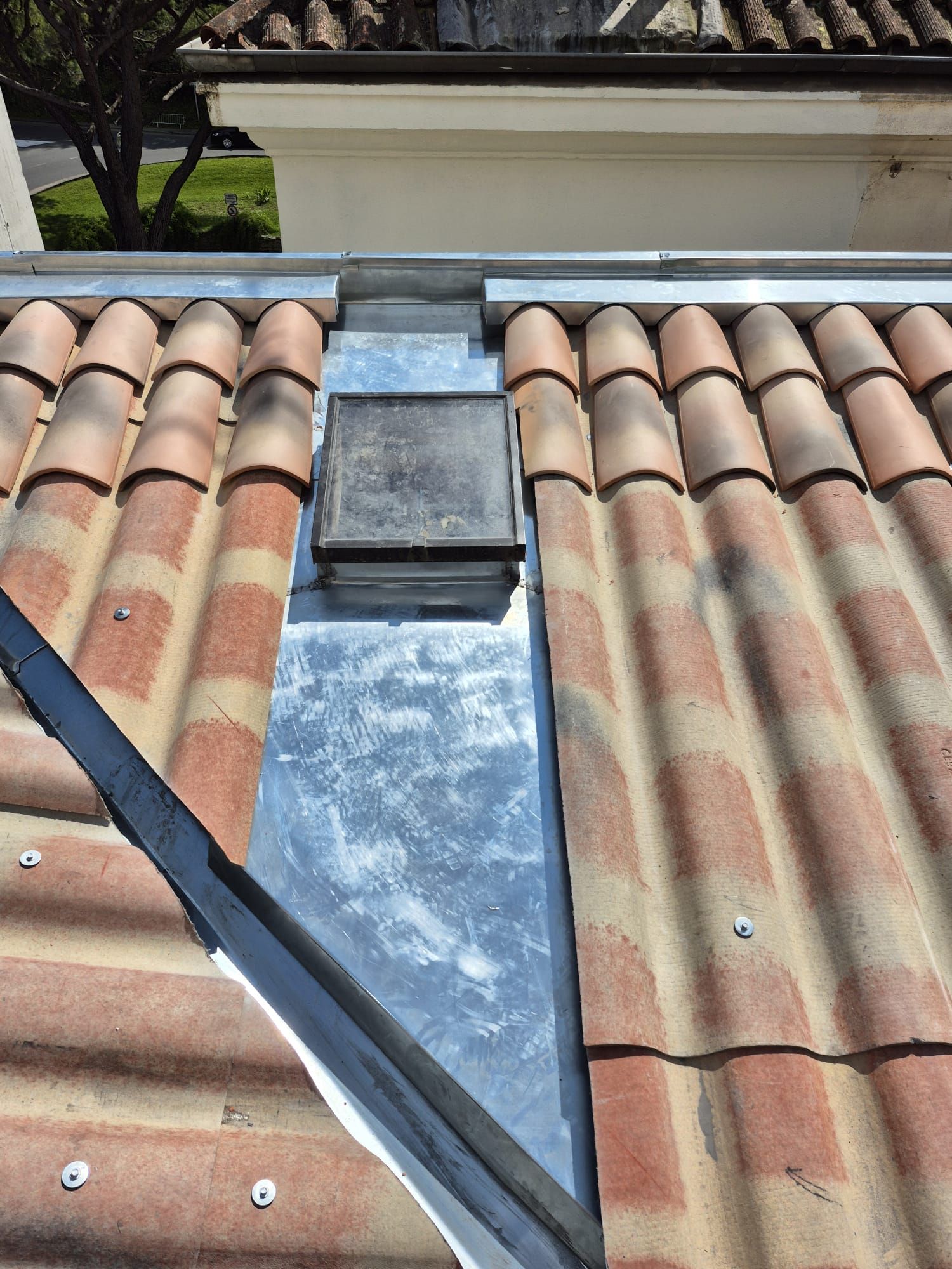 Gros plan sur un toit de tuiles avec un évent recouvert d'une bande métallique.