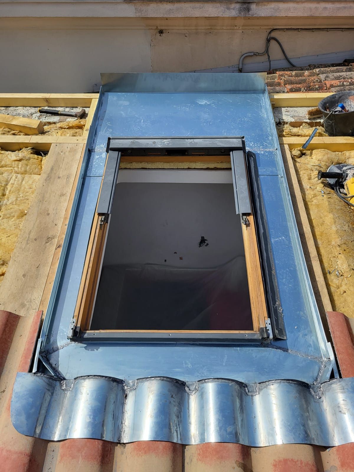 Installation d'un puits de lumière sur un toit avec une bande de solin métallique et une fenêtre partiellement ouverte.